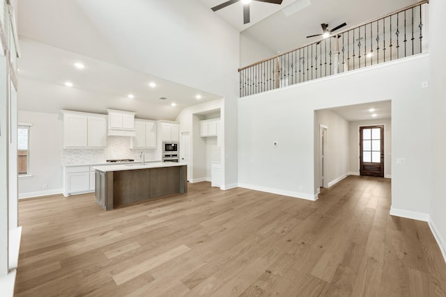 kitchen with white cabinetry, a center island with sink, high vaulted ceiling, and light hardwood / wood-style flooring