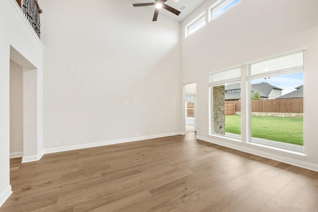 unfurnished living room with wood-type flooring, a towering ceiling, and ceiling fan