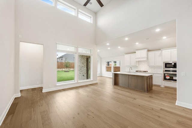 kitchen with a wealth of natural light, stainless steel appliances, white cabinetry, and a kitchen island with sink