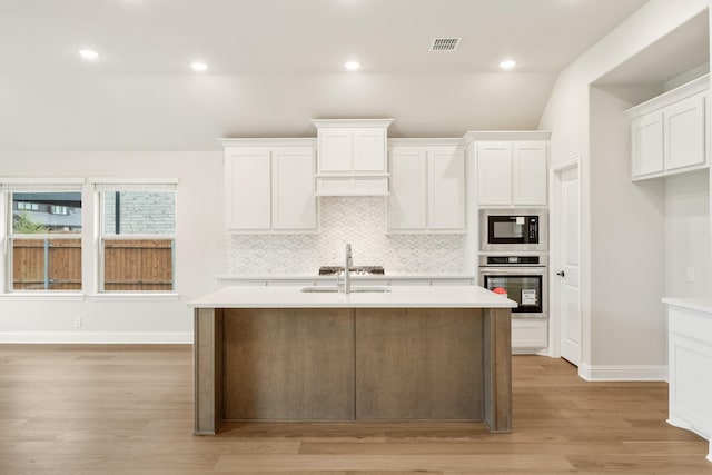 kitchen with white cabinets, light hardwood / wood-style floors, black microwave, and stainless steel oven