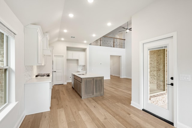 kitchen featuring sink, tasteful backsplash, an island with sink, light hardwood / wood-style floors, and white cabinets