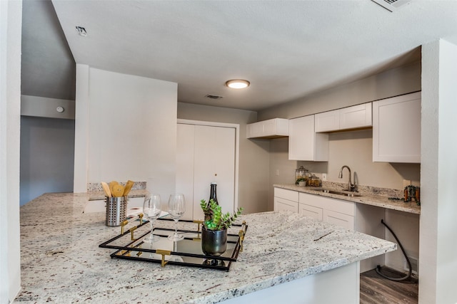 kitchen with wood finished floors, electric cooktop, light stone countertops, white cabinets, and a sink