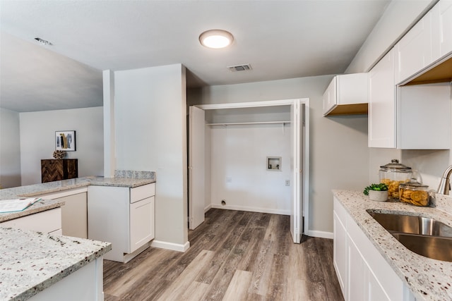 kitchen with light stone counters, white cabinets, hardwood / wood-style flooring, and sink