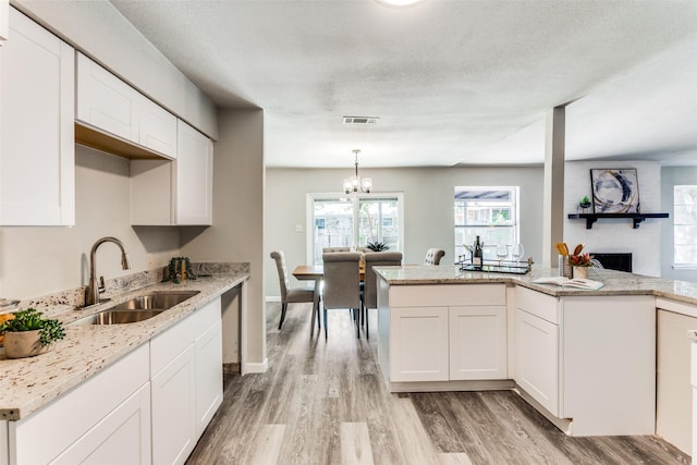 kitchen with visible vents, a fireplace, light wood-type flooring, a sink, and white cabinetry