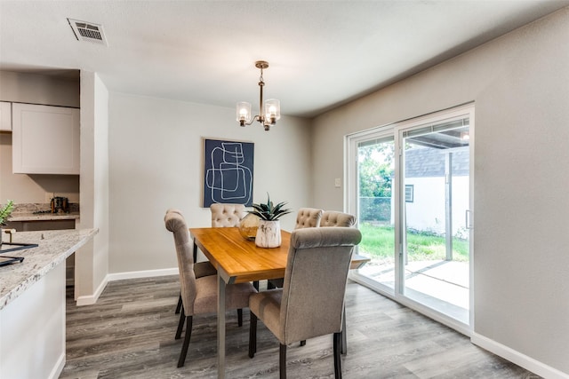 dining room featuring a notable chandelier, baseboards, visible vents, and wood finished floors