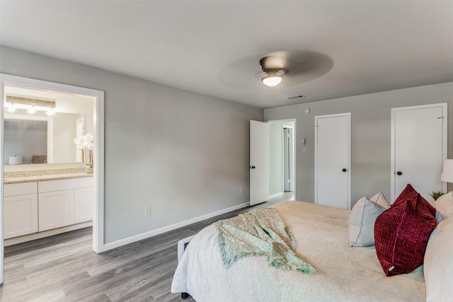 bedroom with visible vents, wood finished floors, baseboards, ceiling fan, and ensuite bath