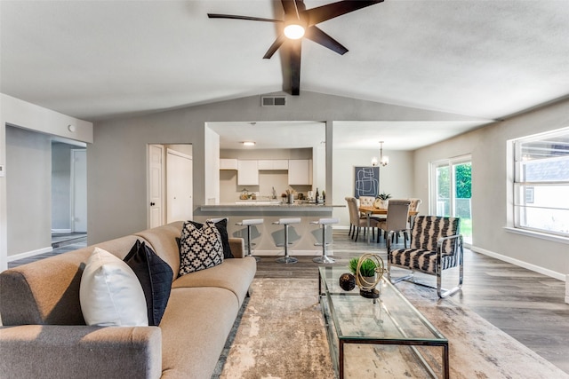 living room with ceiling fan with notable chandelier, baseboards, vaulted ceiling with beams, wood finished floors, and visible vents