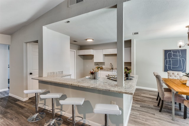 kitchen featuring light stone counters, white cabinets, kitchen peninsula, dark wood-type flooring, and a breakfast bar area