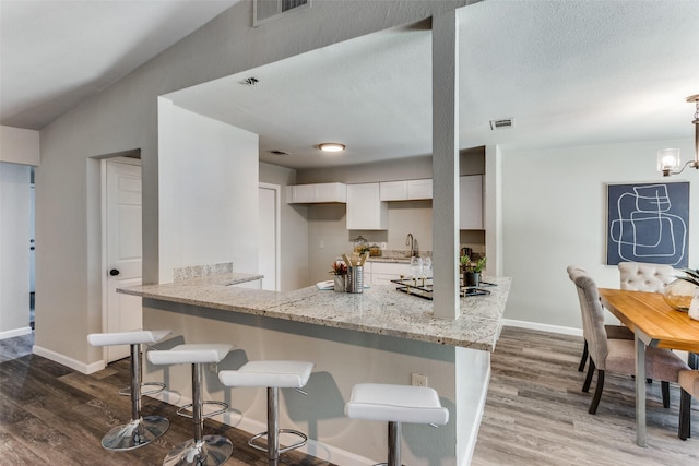 kitchen featuring visible vents, wood finished floors, light stone countertops, baseboards, and white cabinets