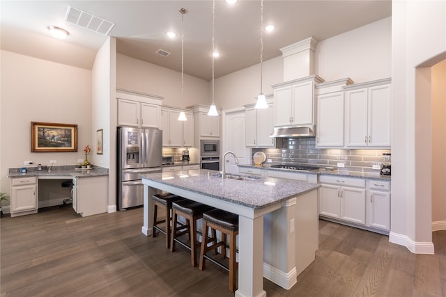 kitchen featuring light stone counters, pendant lighting, stainless steel appliances, a center island with sink, and dark hardwood / wood-style floors