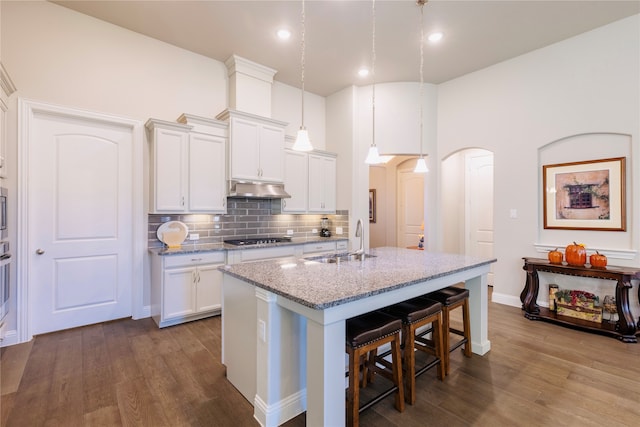 kitchen featuring light stone counters, wood-type flooring, decorative light fixtures, black gas cooktop, and sink