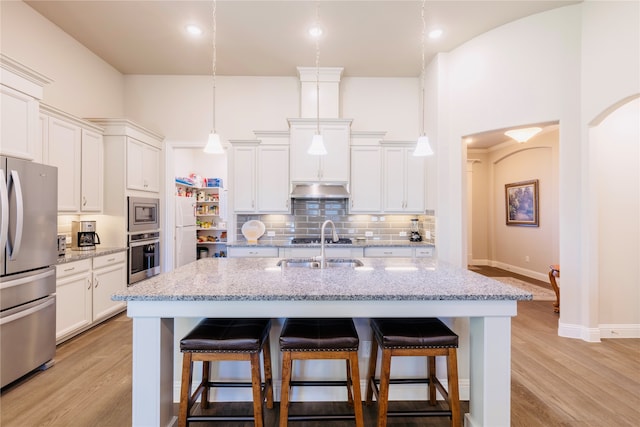 kitchen with a center island with sink, light hardwood / wood-style floors, pendant lighting, and stainless steel appliances