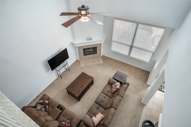 unfurnished living room featuring light carpet, a high ceiling, a tiled fireplace, and ceiling fan