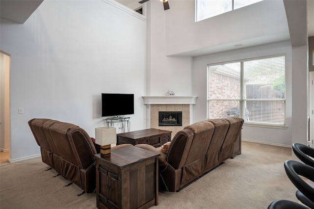 carpeted living room featuring a towering ceiling, ceiling fan, and a tile fireplace