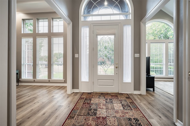 entryway with crown molding, light hardwood / wood-style floors, and a high ceiling