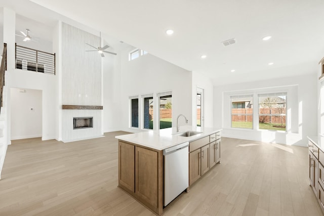 kitchen featuring light wood-type flooring, a towering ceiling, white dishwasher, a center island with sink, and a fireplace