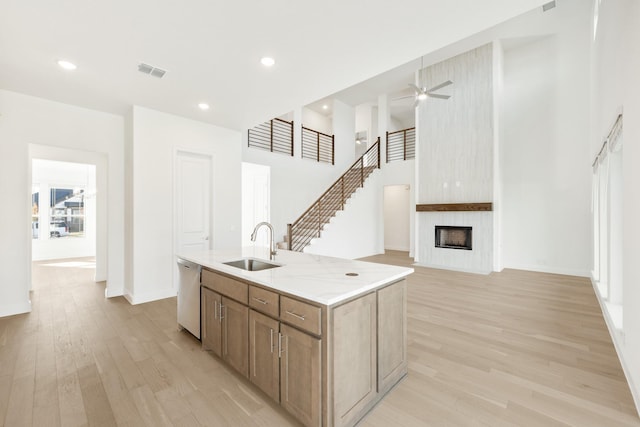 kitchen featuring sink, dishwasher, light hardwood / wood-style flooring, an island with sink, and a fireplace