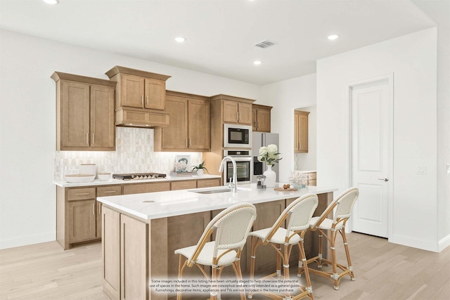 kitchen featuring a kitchen island with sink, sink, stainless steel appliances, and light wood-type flooring