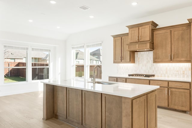 kitchen with light wood-type flooring, a center island with sink, backsplash, and sink