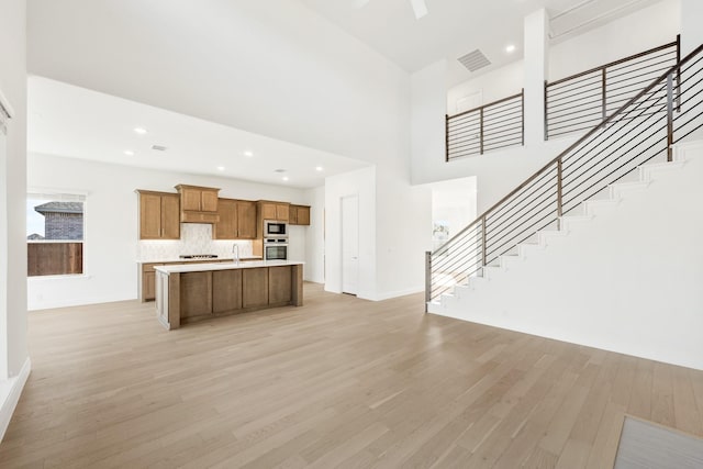 kitchen featuring a towering ceiling, stainless steel appliances, sink, a center island with sink, and light hardwood / wood-style flooring