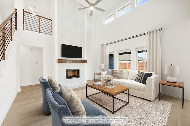 living room featuring ceiling fan, light wood-type flooring, a fireplace, and a towering ceiling