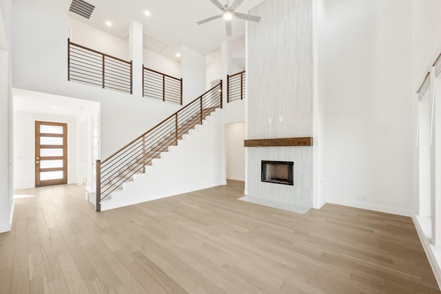 unfurnished living room featuring ceiling fan, light hardwood / wood-style floors, a fireplace, and a high ceiling