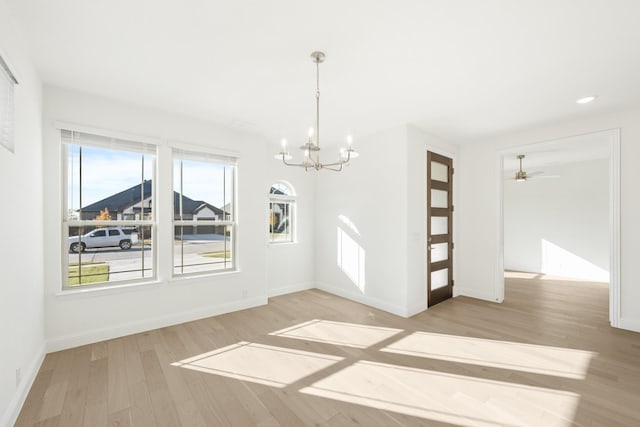 unfurnished dining area featuring light hardwood / wood-style flooring, a healthy amount of sunlight, and ceiling fan with notable chandelier