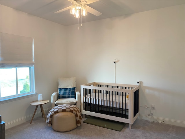 carpeted bedroom featuring ceiling fan and a nursery area