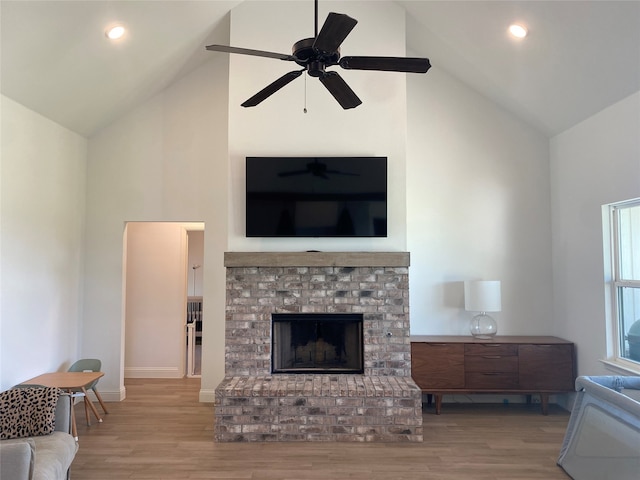 living room featuring ceiling fan, a brick fireplace, light hardwood / wood-style floors, and high vaulted ceiling