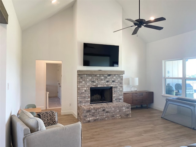 living room featuring ceiling fan, light hardwood / wood-style flooring, a brick fireplace, and high vaulted ceiling