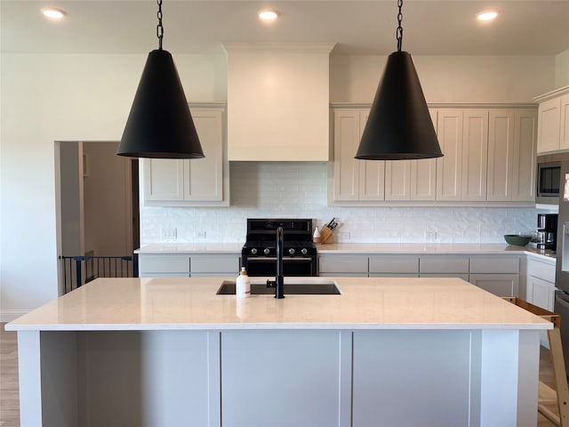 kitchen with black gas stove, light stone counters, a kitchen island with sink, sink, and hardwood / wood-style floors