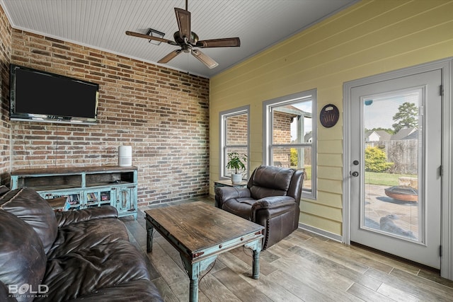 living room featuring ceiling fan, light wood-type flooring, crown molding, and brick wall