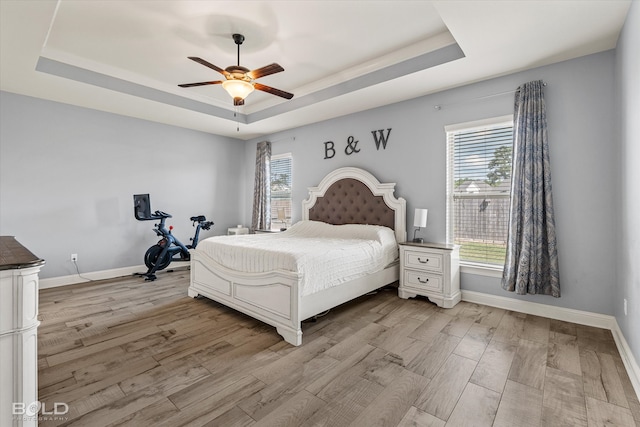 bedroom with a tray ceiling, light hardwood / wood-style floors, and ceiling fan