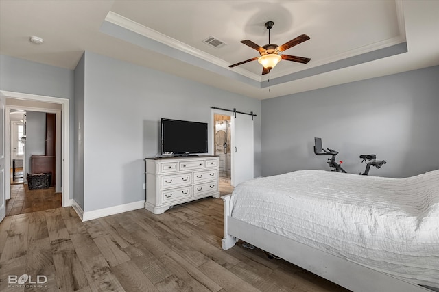 bedroom with light hardwood / wood-style flooring, a raised ceiling, and a barn door