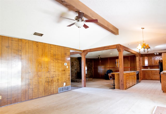 unfurnished living room featuring ceiling fan with notable chandelier, wood walls, lofted ceiling with beams, and light carpet