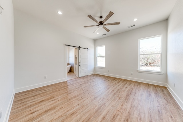 unfurnished bedroom featuring ceiling fan, ensuite bathroom, light hardwood / wood-style floors, and a barn door