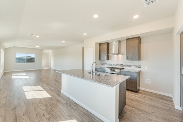 kitchen with a kitchen island with sink, wall chimney range hood, sink, light stone counters, and light hardwood / wood-style floors