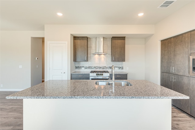 kitchen featuring wall chimney range hood, light hardwood / wood-style flooring, and an island with sink