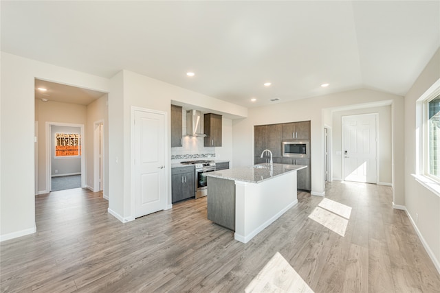 kitchen featuring wall chimney exhaust hood, stainless steel appliances, a center island with sink, sink, and light wood-type flooring