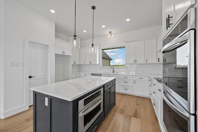 kitchen with hanging light fixtures, light hardwood / wood-style floors, a center island, and white cabinets