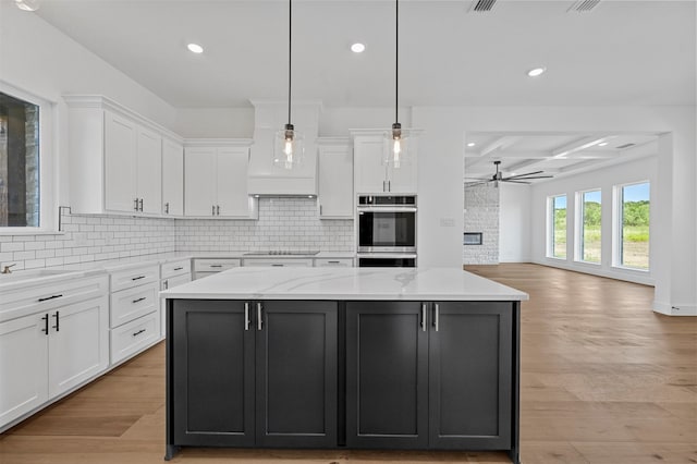 kitchen with a kitchen island, decorative light fixtures, white cabinetry, double oven, and light wood-type flooring