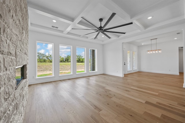 unfurnished living room with light wood-type flooring, ceiling fan with notable chandelier, beam ceiling, and a wealth of natural light