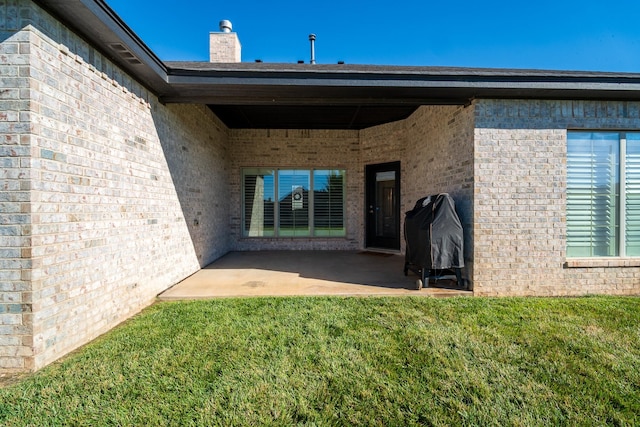 rear view of property with a chimney, a patio, a yard, and brick siding