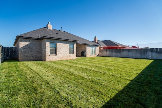 rear view of house featuring brick siding, a fenced backyard, a lawn, and a chimney
