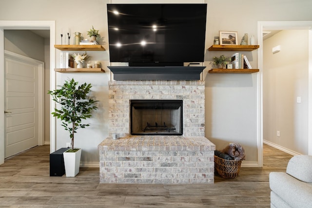 living area featuring a brick fireplace, baseboards, and wood finished floors