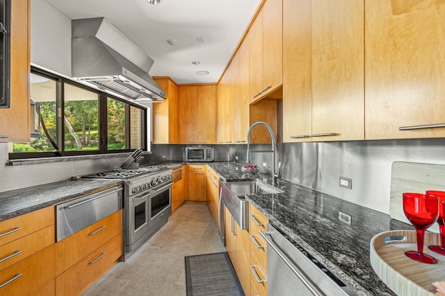 kitchen featuring dark stone countertops, backsplash, wall chimney range hood, a sink, and appliances with stainless steel finishes