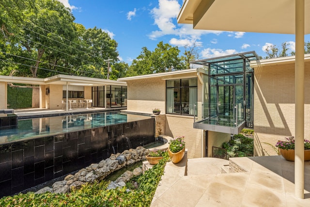 back of property featuring brick siding, an outdoor pool, a patio, and stucco siding