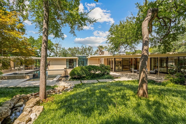 back of property featuring a lawn, an outdoor pool, and a patio area