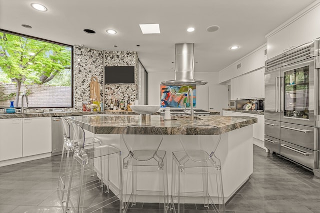 kitchen with white cabinets, a kitchen island, built in refrigerator, dark stone countertops, and a breakfast bar area