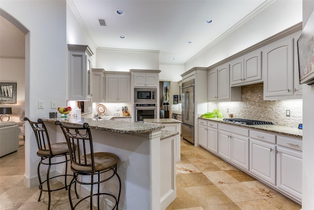 kitchen with a breakfast bar area, appliances with stainless steel finishes, backsplash, light stone counters, and ornamental molding